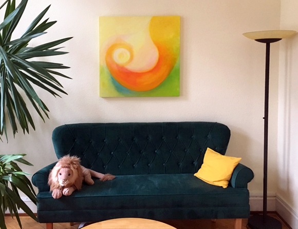 Ein dunkelgrünes Samt-Sofa mit einem Kissen und einem Stofftier. Darüber eine Gemälde.